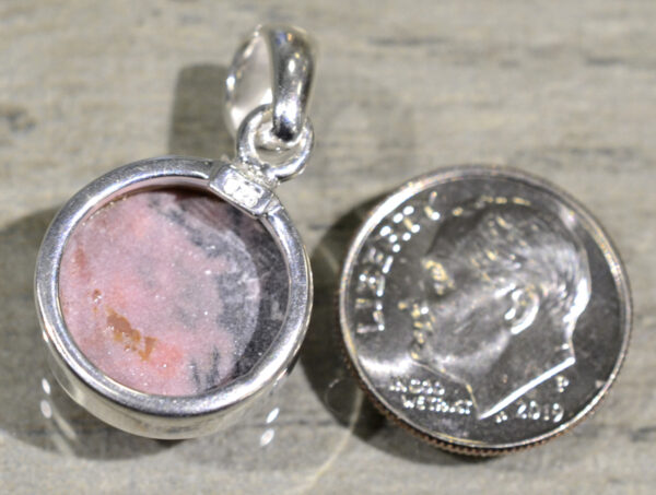 back of pink rhodonite circle shaped pendant with dime for scale